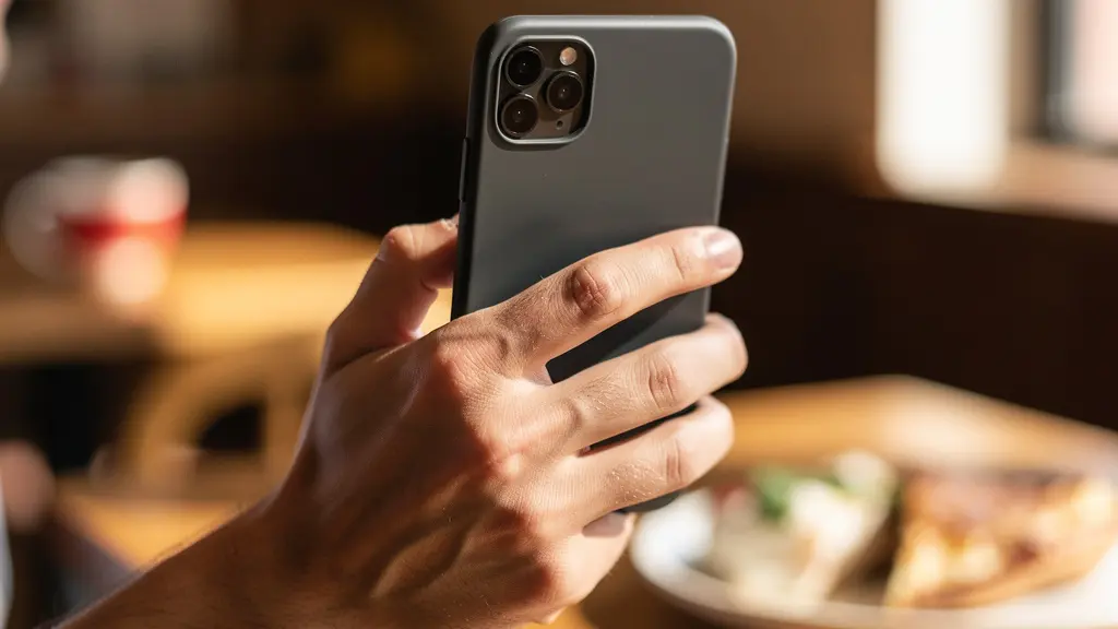 Plan serré sur une main tenant un smartphone pour photographier une assiette dans un restaurant, sans écran visible.